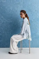 Camisa de calce relajado con cuello clásico, mangas largas con puños elastizados y rayas verticales que aportan un estilo atemporal. Su diseño liviano y versátil cuenta con estampado floral verde sobre fondo de rayas celestes y blancas.