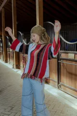 Sweater tejido en hilado 100% algodón con diseño a rayas verticales en tonos rojo, blanco, marrón y negro. Presenta flecos en el ruedo y bordados en el escote.