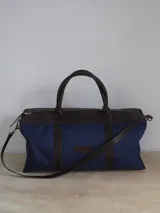 Bolso de lona color verde militar con detalles en cuero marrón. Tiene doble asa de mano y correa de hombro ajustable y extraíble.