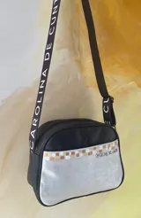 Bandolera de cuero negro y plateado con arte pintado a mano, perteneciente a la línea Ottenta de Carolina De Cunto. Cuenta con bolsillo frontal exterior, cierre superior con cremallera, forro interior con bolsillo y correa regulable con el logo de la marca.