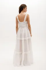 Vestido largo blanco de gasa de algodón con textura liviana. Tiene escote en V con nudo central, breteles con voladitos y falda con frunces.