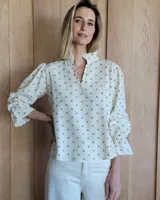 Blusa de algodón con estampado de lunares, cuello alto con volados y escote en V. Presenta mangas largas abullonadas con puños elásticos y terminación con volados.