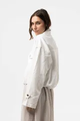 Campera de denim liviano oversize color blanco, con cuello alto, cierre frontal con botones y bolsillos delanteros con solapa. Presenta pespuntes en contraste y una silueta relajada.