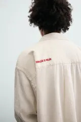 Camisa de corte relajado confeccionada en tejido con mezcla de lino. Presenta cuello solapa, manga larga con puños abotonados, bolsillo plastrón en el pecho y cierre frontal con botones. Incluye bordados a contraste en la espalda.
