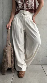 Pantalón palazo de lino color beige, de calce amplio y fluido, con tablas en el frente, botón, cierre y cordón ajustable en la cintura.