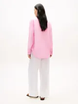 Camisa de lino puro de corte amplio color rosado, con cuello inglés, mangas largas con puños abotonados, bajo camisero y logo bordado en el pecho.