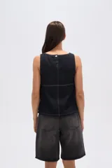 Musculosa de jean azul oscuro, de corte holgado, con cuello bote, pespuntes blancos y cierre lateral con botones metálicos.