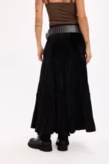 Falda larga de color negro con textura símil terciopelo, presenta un diseño con volados y detalle de tachas en la cintura.