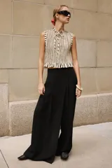 Pantalón negro de tiro alto con diseño cruzado tipo pareo, pinzas delanteras y pernera ancha. Cuenta con cierre lateral de cremallera oculta.