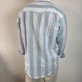 Camisa de manga larga con cuello mao, confeccionada en tejido de lino a rayas verticales en tonos blanco y celeste. Presenta cierre frontal con botones y corte clásico.
