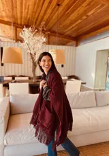 Ruana tejida color borgoña con flecos y bolsillos.