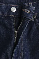 Jean de tiro alto con corte mom slim fit, confeccionado en denim azul oscuro con costuras en contraste. Presenta diseño de cinco bolsillos, cierre con botón y pierna recta con largo al tobillo.