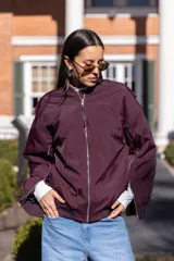 Campera bomber oversize color borgoña de nylon con cierre frontal, bolsillos laterales con cierre, puños y cuello tejidos al tono.