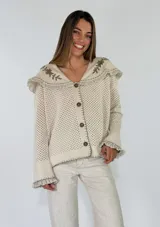 Saco tejido de punto color azul con diseño calado, cuello grande con bordados florales en tono crudo, volados decorativos y cierre frontal con un botón.