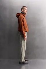 Chaqueta de hombre color marrón óxido con textura de pequeños cuadrados en relieve. Presenta cierre frontal de cremallera, capucha ajustable, bolsillos laterales con solapa y puños ajustables. El interior es de forro polar.