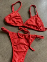 Conjunto de bikini de textura acanalada en color rojo vibrante. El corpiño es de estilo triangular con breteles regulables, y la bombacha es de corte cavado con tiras laterales ajustables para anudar.