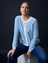 Cardigan de tejido tweed celeste y blanco, con escote redondo, cierre frontal con botones metálicos dorados y bolsillos simulados en el frente.