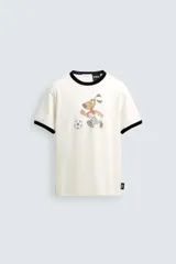 Camiseta de algodón color crudo con cuello y bordes de mangas en contraste negro. Presenta un estampado frontal de estilo vintage con el personaje Striker, mascota de la Copa Mundial de la FIFA 1994, jugando al fútbol.