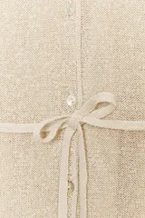 Chaqueta de punto color beige claro, con escote en V, manga larga y cierre frontal de botones. Presenta un cinturón fino del mismo tejido anudado a la cintura.
