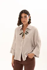 Camisa de textura plisada en color beige, con cuello clásico, cierre frontal de botones y mangas tres cuartos con puños vueltos.