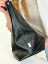Cartera tote de cuero genuino color negro, con costuras visibles a contratono, asas dobles para hombro, parche frontal con logo grabado y charms colgantes en forma de estrella y mini monedero.