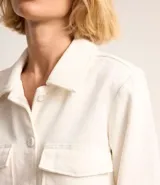 Campera corta color blanco hueso, estilo trucker, con cuello clásico, cierre abotonado, bolsillos cargo con solapa en el pecho y mangas largas con puños abotonados.