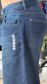 Pantalón de jean azul oscuro de corte wide leg, con diseño holgado y tiro medio. Presenta un pequeño bordado con alas en el bolsillo delantero.