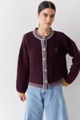 Cardigan de punto color bordó con cuello redondo, cierre frontal de botones y detalles de ribetes en contraste en cuello, puños y ruedo. Presenta un pequeño bordado de una raqueta de tenis en el pecho.