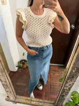 Chaleco de hilo color beige, con diseño de tejido calado, cuello redondo y volados en las sisas.