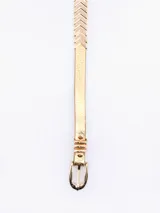 Cinto fino de cuero sintético en color dorado metalizado, con hebilla metálica a tono y pasador decorativo.