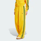 Pantalón deportivo Adidas de corte holgado, color amarillo brillante con las clásicas tres tiras verdes en los laterales y el logo del trifolio bordado en la pierna izquierda. Cuenta con cintura elástica y bolsillos laterales con cierre.
