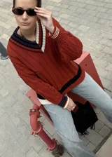 Buzo tejido de punto con escote en V, manga larga y diseño holgado. Presenta un patrón de rayas verticales en relieve y detalles de franjas en contraste en el cuello, puños y ruedo. Incluye un pequeño bordado en el pecho.