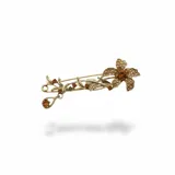 Broche de metal dorado con diseño de flor y tallo decorado con cristales en tonos ámbar y marrones.