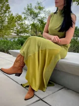 Vestido largo de corte recto y sin mangas, con cuello alto y una abertura lateral pronunciada en la falda. Presenta una textura suave tipo gamuza en color verde oliva.