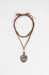 Collar de cordón marrón con dije de escudo plateado con detalles grabados y sol en la parte superior.