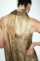 Top sin mangas con cuello tipo choker y escote en pico con lazada frontal. Presenta un diseño con efecto tie-dye en tonos tierra y cierre posterior con abertura y botón.
