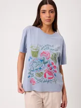 Remera celeste de corte holgado, con cuello redondo, manga corta y estampado frontal colorido de temática costera.