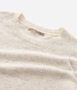 Suéter de punto color beige con cuello redondo, manga larga y aplicaciones de perlas distribuidas por toda la prenda. Presenta puños y ruedo acanalados.