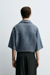 Camisa polo de calce relajado confeccionada en tejido de lino color azul. Presenta cuello solapa con abertura frontal en V y manga corta.