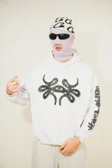 Hoodie blanco con pasamontañas negro incorporado, corte oversize, estampado en el pecho y mangas, y bolsillo tipo canguro.