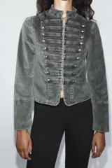 Chaqueta entallada de terciopelo color gris con efecto acid wash, cuello subido, manga larga y cierre frontal con ganchos metálicos. Presenta detalles de pasamanería con falsos botones en el delantero de inspiración militar.