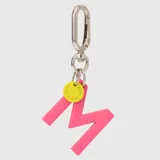 Llavero con dije en forma de letra A color rosado y pequeño dije circular amarillo con logo de la marca grabado. Incluye gancho metálico tipo mosquetón.