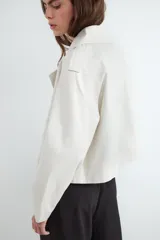 Campera estilo trench corta color beige, con solapas amplias, cierre cruzado de doble botonadura con botones oscuros y diseño holgado.