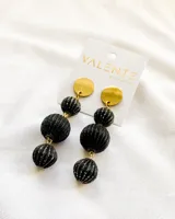 Aros colgantes con base circular dorada y tres esferas texturizadas negras con detalles plateados.