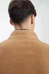 Buzo de hombre con cierre frontal, confeccionado en tejido sherpa color camel, con paneles superiores en verde oliva acolchado y cuello alto en color beige.