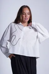 Camisa negra de manga larga con cuello clásico y cierre frontal con botones. Presenta bordados abstractos en blanco y negro en el frente.