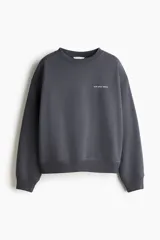 Buzo oversize gris oscuro con cuello redondo, hombros caídos y pequeño texto estampado en el pecho. Presenta puños y bajo con ribete acanalado.