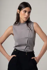Top sin mangas de tejido de punto fino en color gris, con cuello alto y cierre frontal decorativo mediante nudos de estilo oriental.