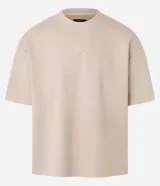 Remera oversized color beige confeccionada en gamuza sintética. Presenta cuello redondo, mangas cortas y bordado de cruz en el frente.