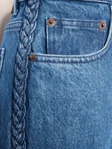 Pantalón de jean azul de tiro medio y corte recto, con terminación desflecada y detalles de trenzas en los laterales.